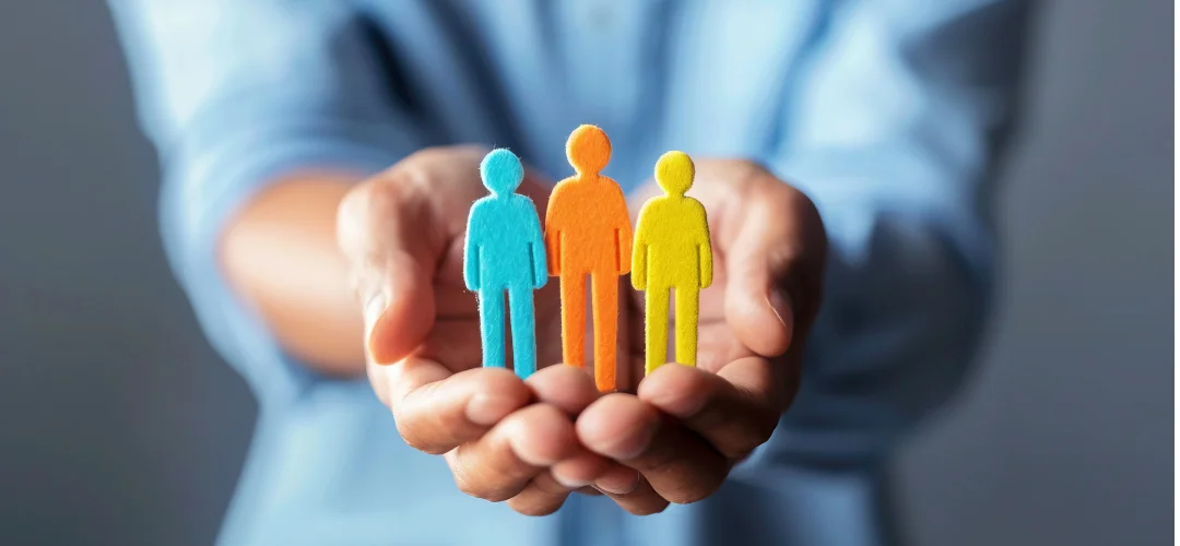 Manos sosteniendo tres figuras de personas de colores